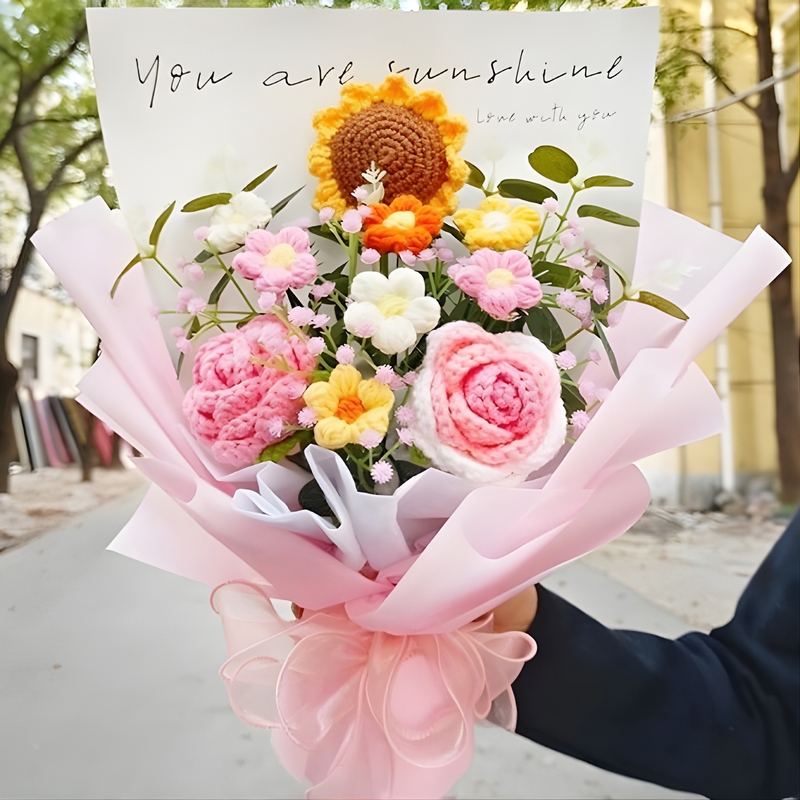 Bouquet of knitted flowers with a card reading 'You are sunshine' held outdoors.